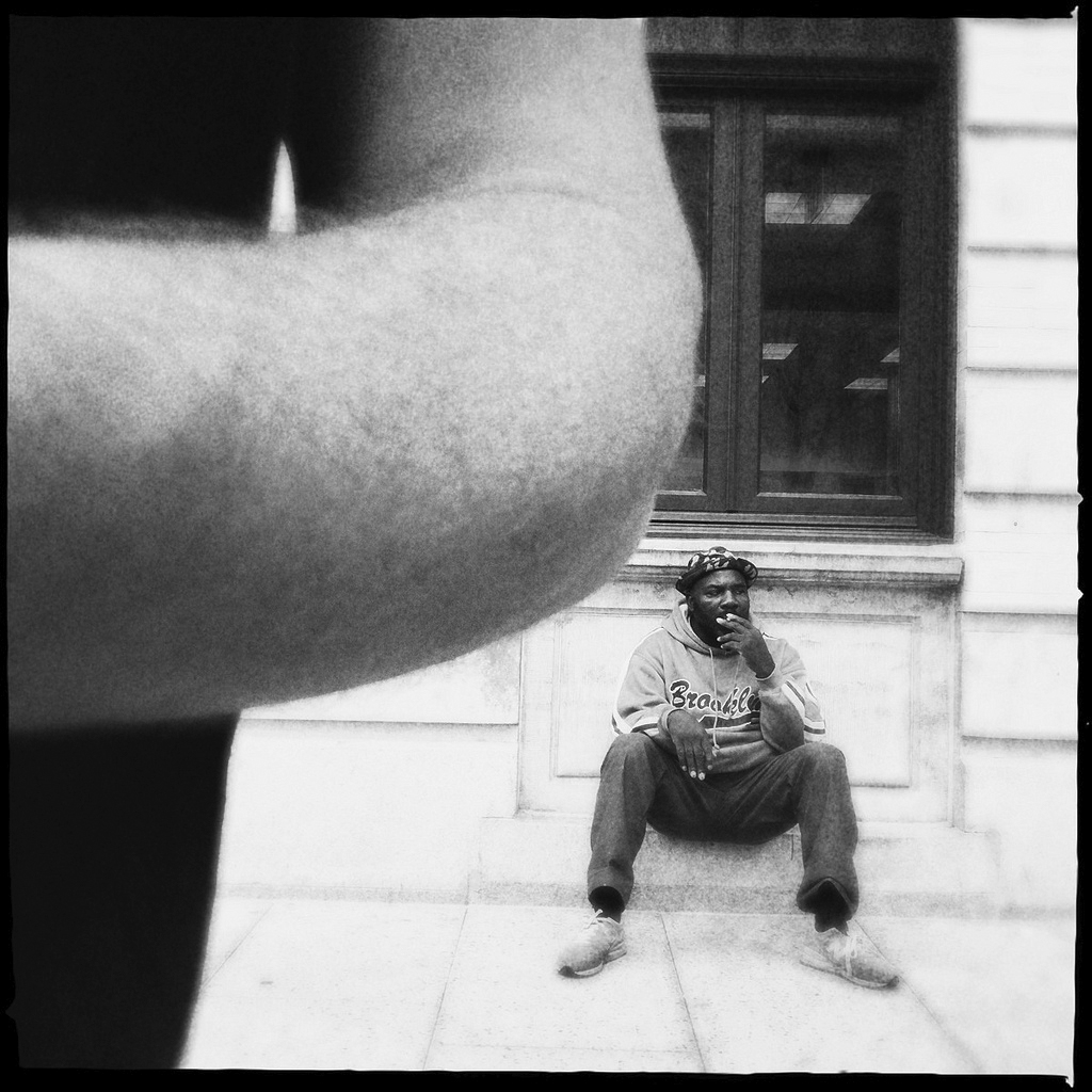 a photo of a black man who is sitting on the street and smoking