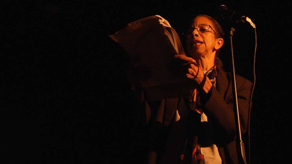Photo of Angie reading poetry in front of a microphone.