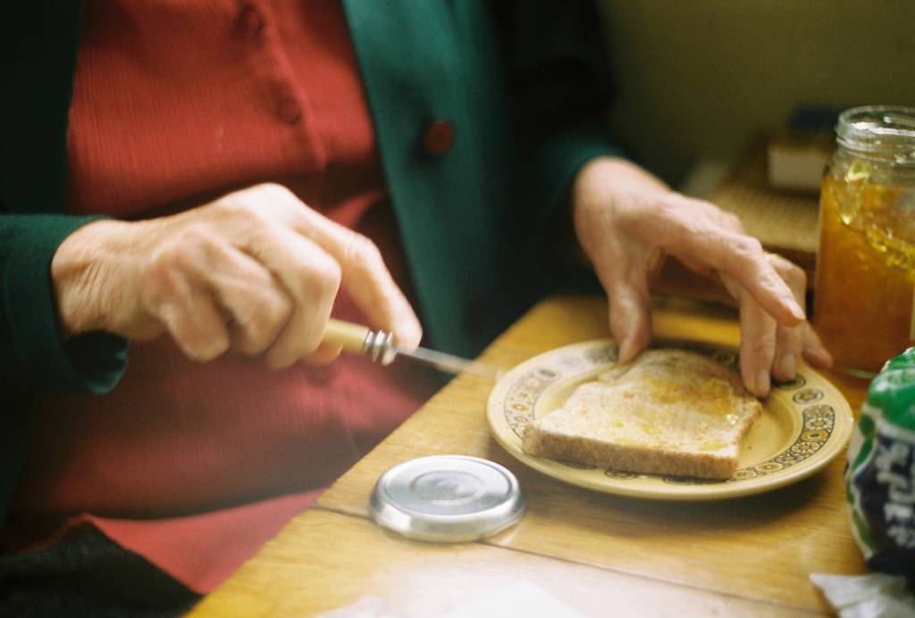Elderly person spreading marmalade on toast.