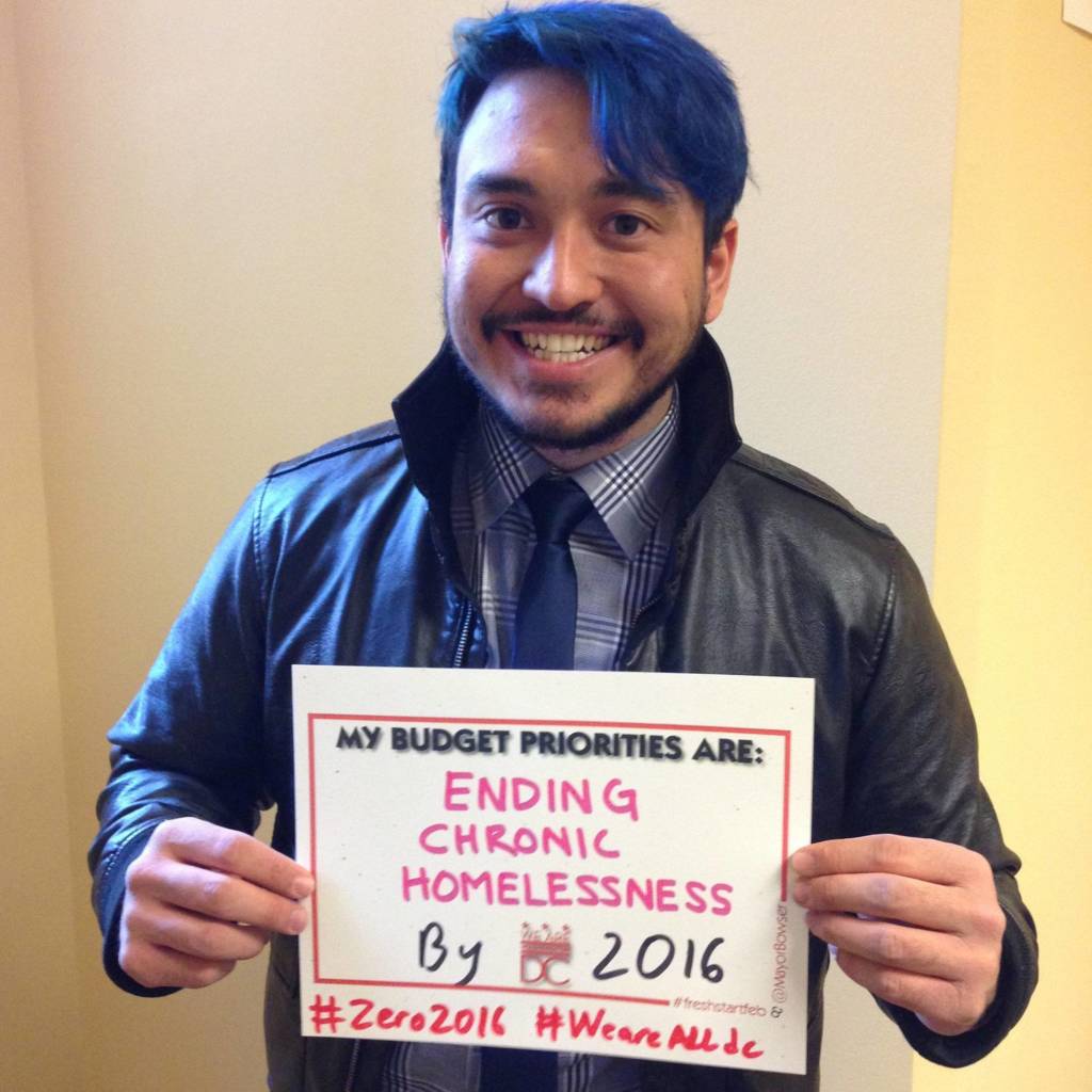 Man holding a sign that says "my budget priorities are ending chronic homelessness by 2016."