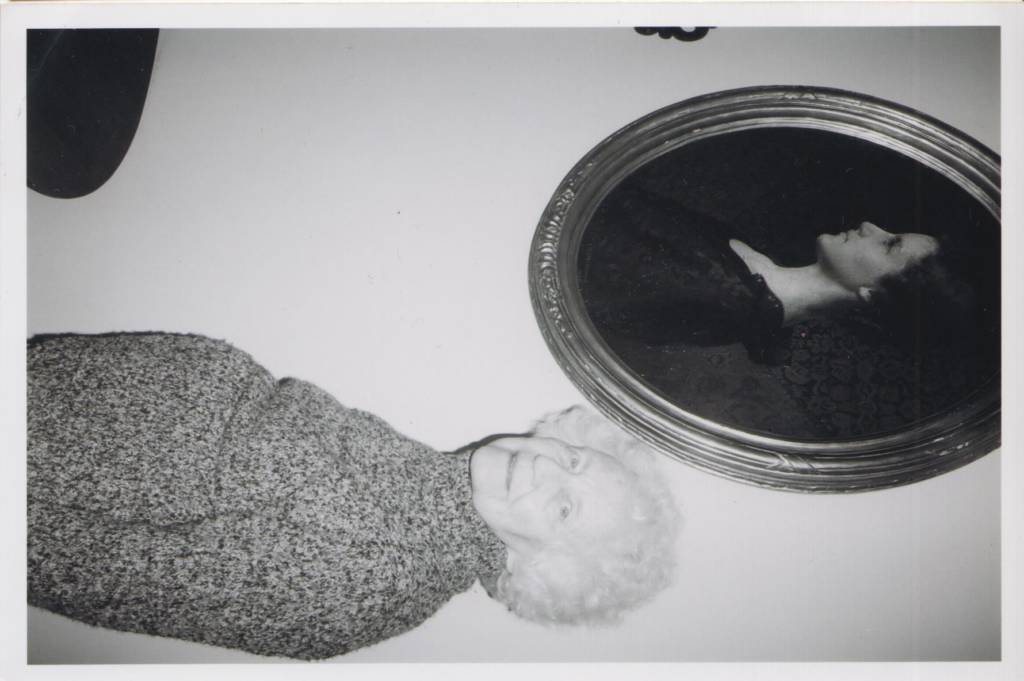 Old woman standing next to a picture or her younger self