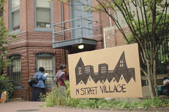Image of a sign that has a drawing of a village with the words "N Street Village."