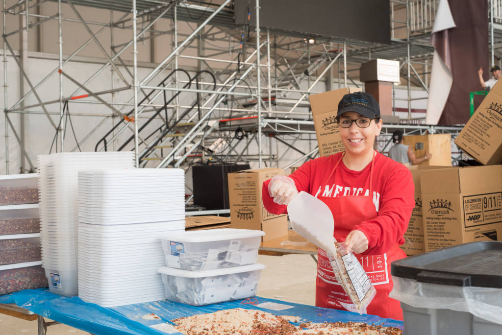 A woman in a red apron packages food into a plastic bag.