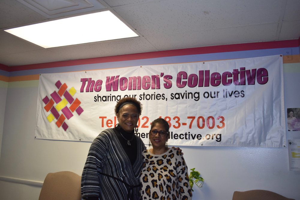Angela Hodges and Patricia Nalls pose in front of the Women's Collective sign, which reads "Sharing our stories, saving our lives."