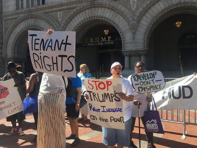 Several demonstrators holding signs in front of the Trump International Hotel.