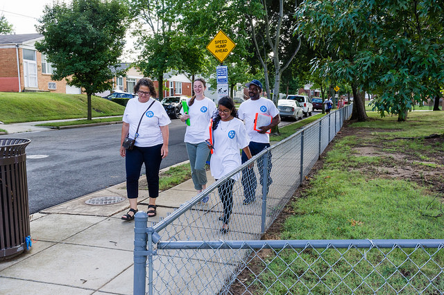 Freya Speilberg and her team walk along a fence in the Benning Terrace neighborhood in Urgent Wellness white T-shirts