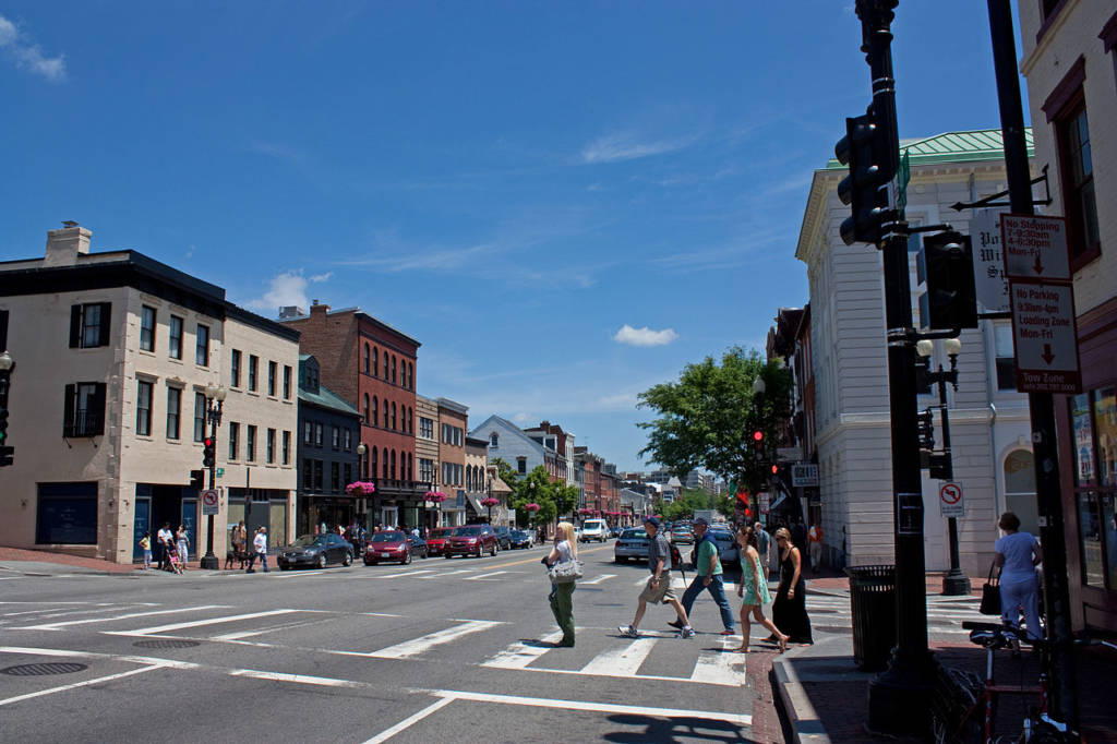 People cross M Street with buildings in the background.