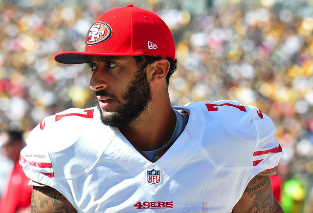 Colin Kaepernick in football pads and a baseball cap.