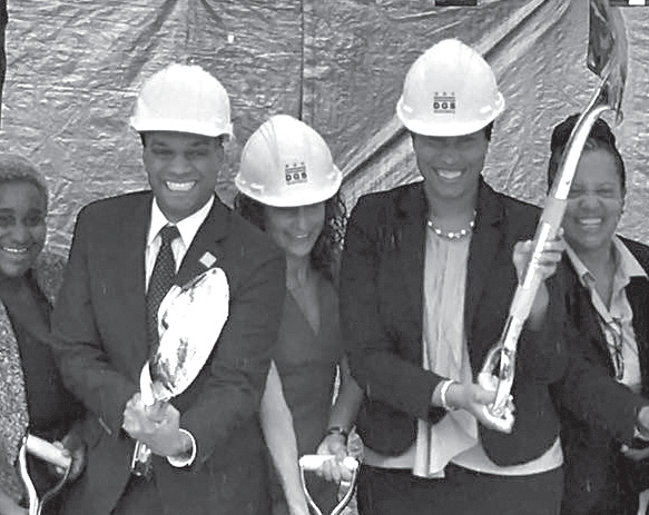 People in suites and hardhats hold shovels triumphantly.