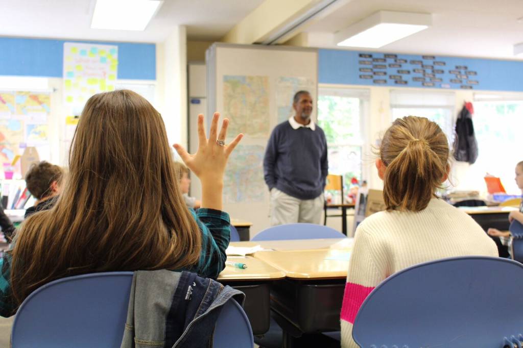 student raising hand with man in background