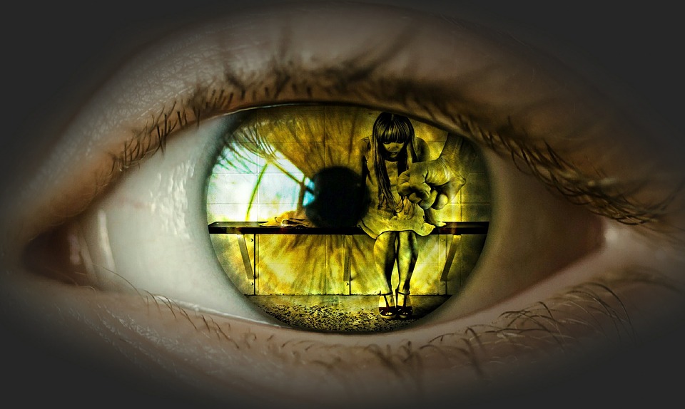 An eye reflects the image of a woman shrinking away from a fist.