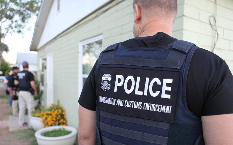 An ICE agent stares off into the distance at other ICE agents.