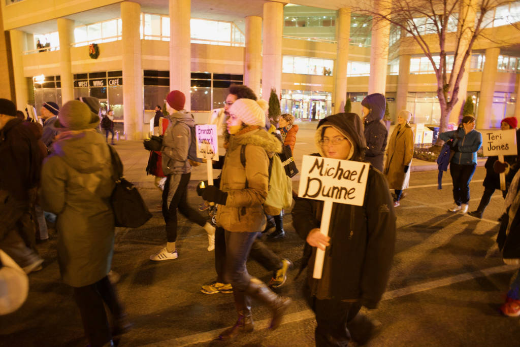 Photo of demonstrators participating in a march. One holds a placard displaying the name "Michael Dunne"