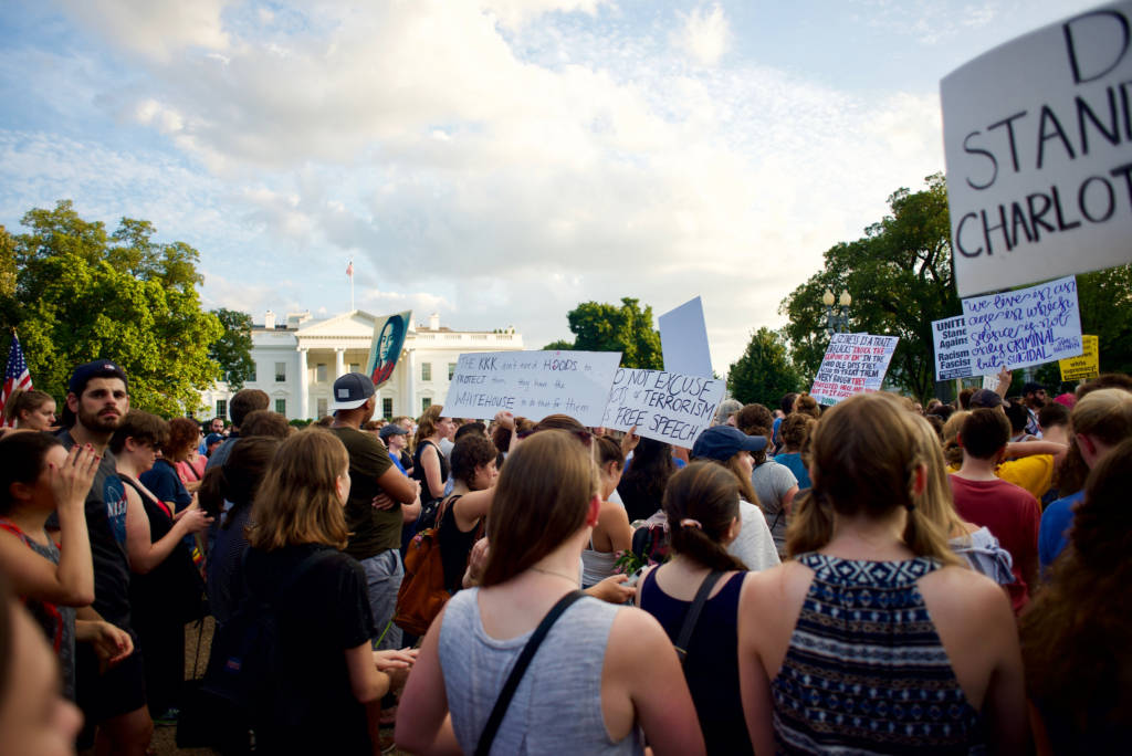 A crowd of protesters holding signs, including one reading "Don't stand with Charlottesville." The White House is in front of them.