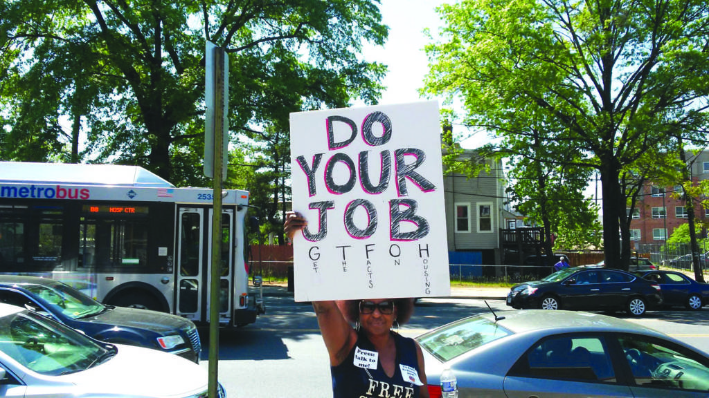 March participant holds a sign that says "DO YOUR JOB. Get the facts on housing."