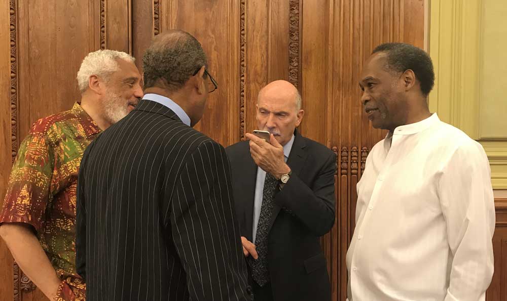 Photo of four men standing together and talking. Phil Mendelson is in the center of the photo, speaking into his phone.