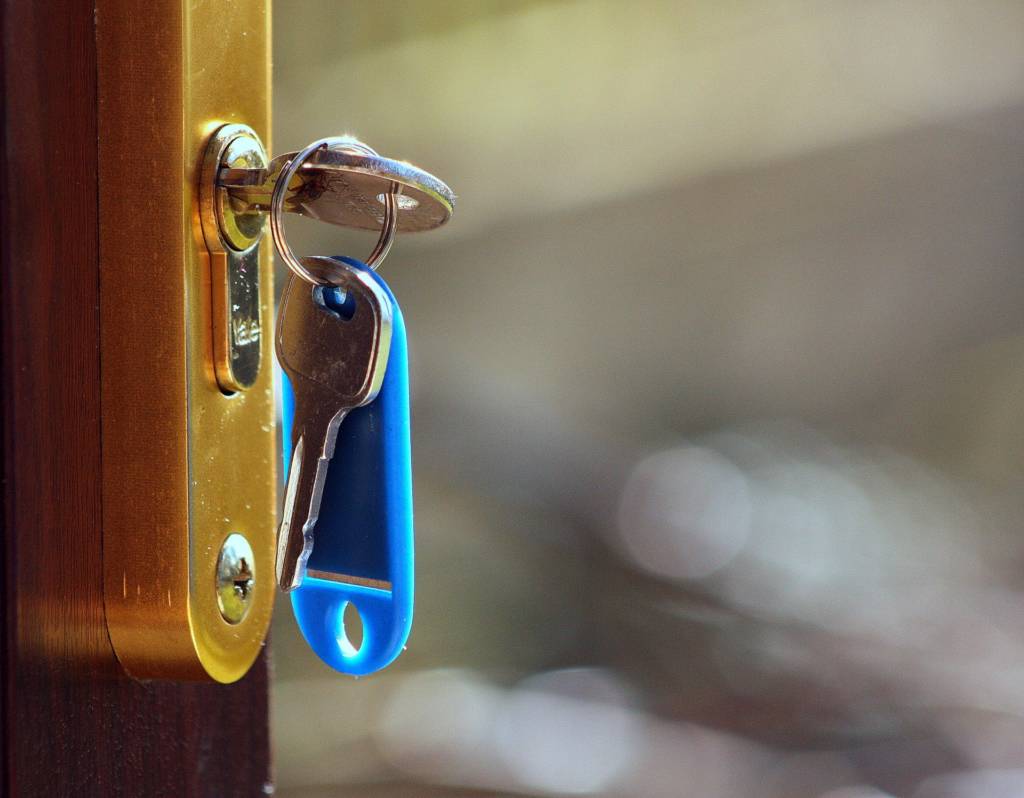 Image of two silver keys one of which is pushed into the key hole in the door.