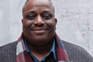 A photo of Leonard Hyater Jr, wearing a blue collared shirt, gray sweater and checkered scarf.