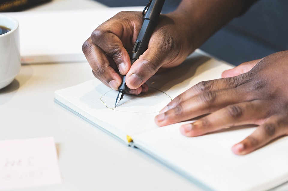 A photograph of hands writing in a notebook.