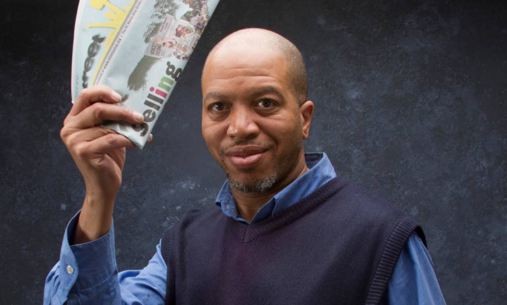 Jeffery McNeil holding a Street Sense Media paper above his head