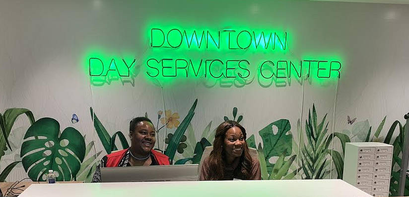 A photo of two women sitting at a desk under a green neon sign is on the wall behind them.