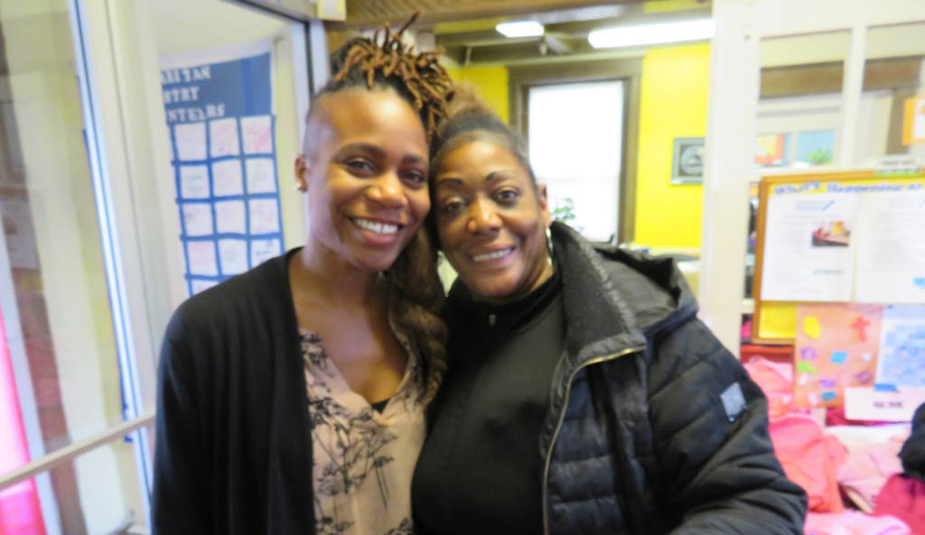 Photo of two women, side-by-side, smiling together in a brightly painted room.