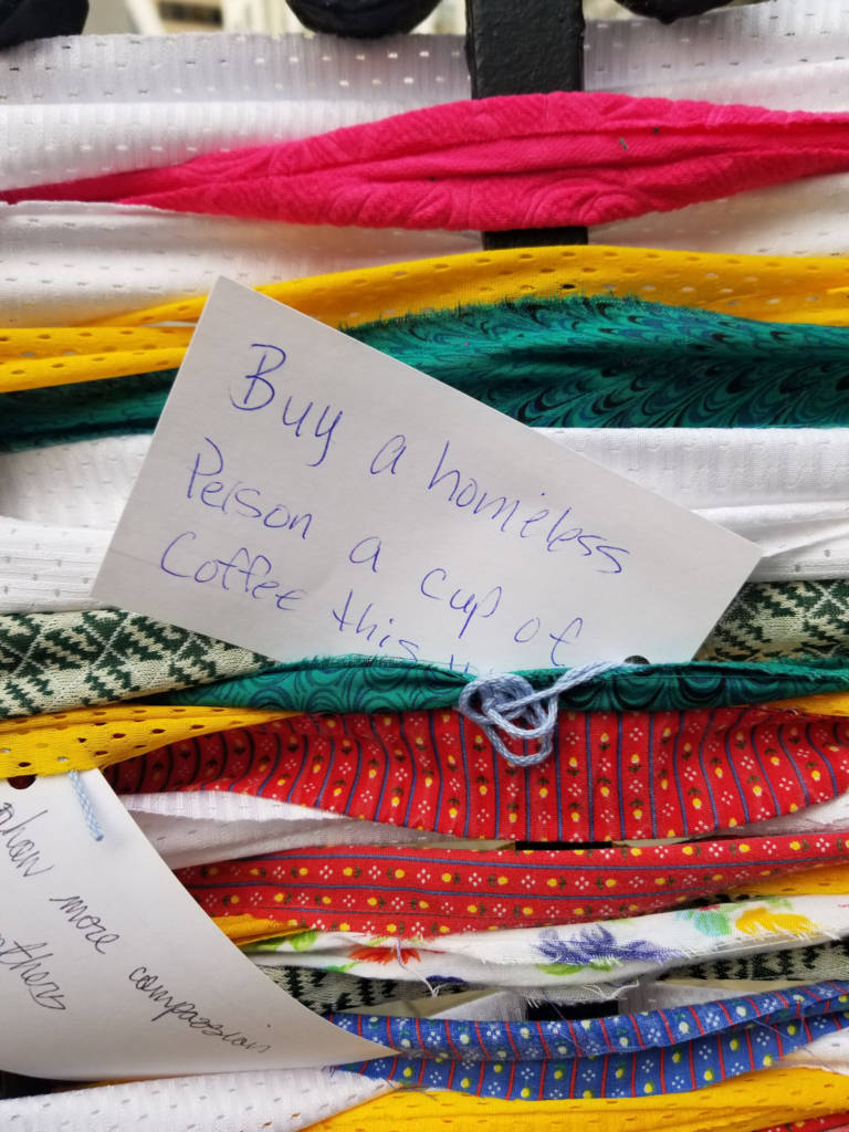 A white index cards that says, "Buy a homeless person a cup of coffee."