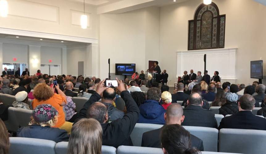 Color photo of Mayor Muriel Bowser speaking to a large group of people in a church.