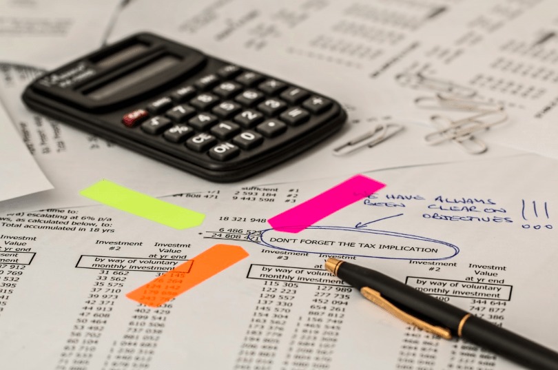 Color photo of paperwork with lots of numbers, a pen, and a calculator
