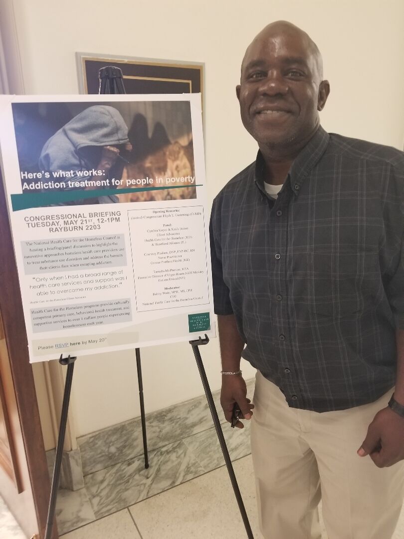 Photo of Keith Belton next to a poster about substance abuse
