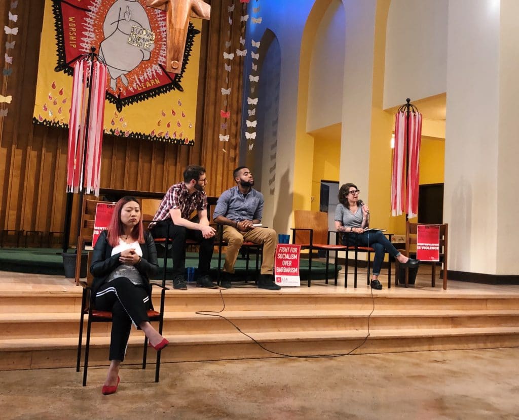 Photo of people sitting in chairs on stairs in a large room with colorful banners.