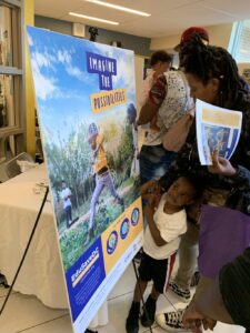 Child standing looking up at EduSaveDC poster with his mother.