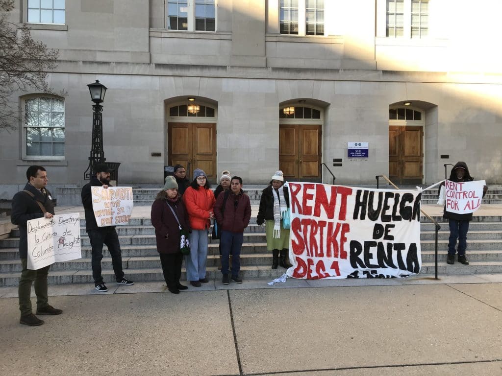 Photo of eight people holding signs including a large banner that says "Rent Strike" in both English and Spanish.