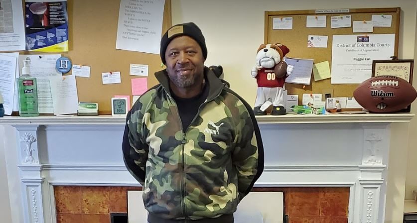 Photo of an African-American man standing in front of a fireplace in his office.