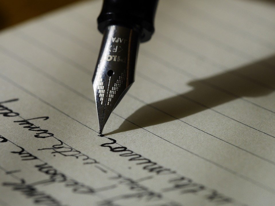 A pen writes on a piece of lined paper.