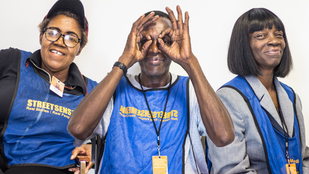 Photo of two women and one man wearing blue Street Sense Media vests with their orange Street Sense Media badges visible.