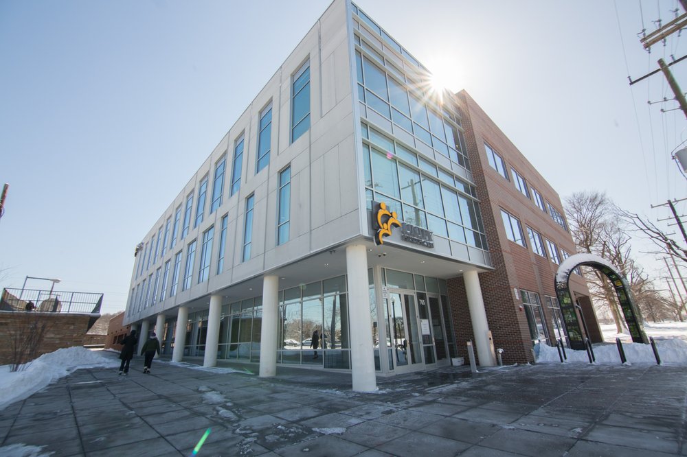 Photo of a building with glass windows. A glint of sun is seen in the top right corner of the image.