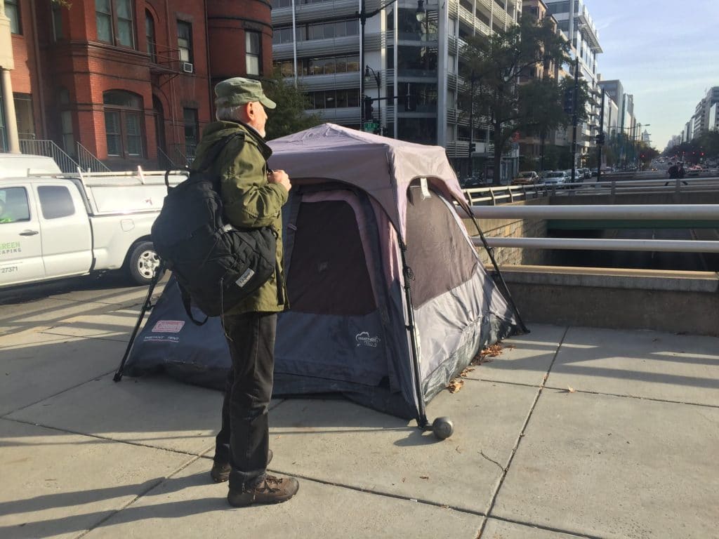 A man standing outside a tent talking to a homeless resident about their situation.