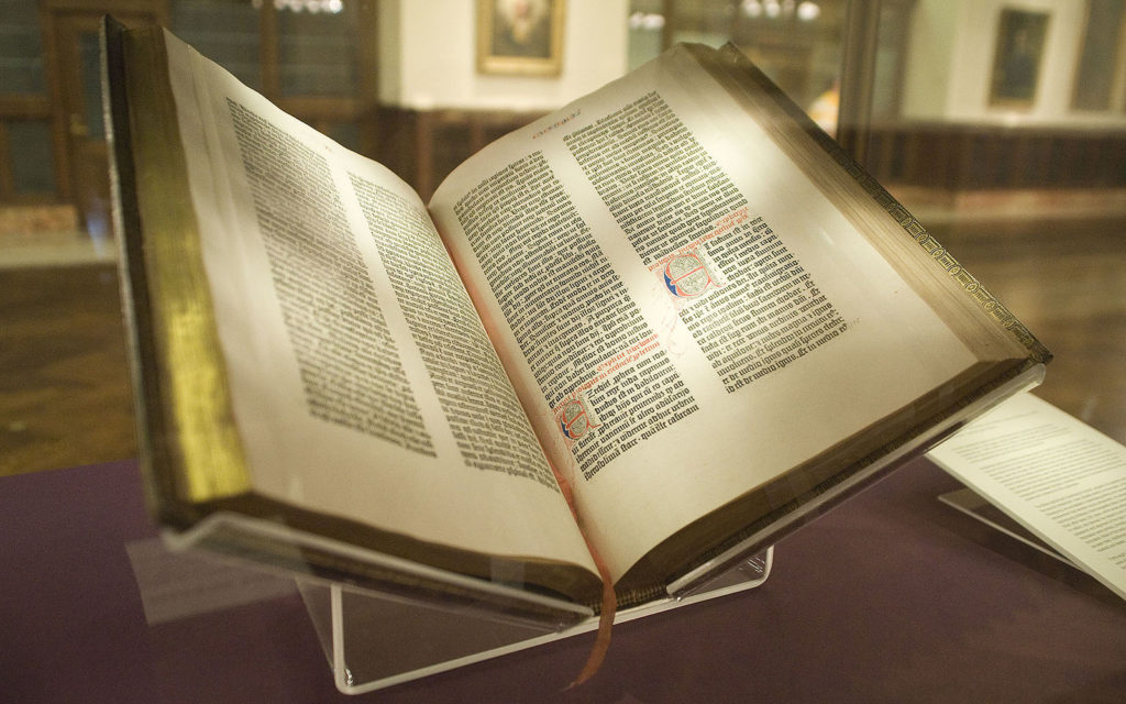 A photo of the Bible propped open. It is lit by an overhead light.