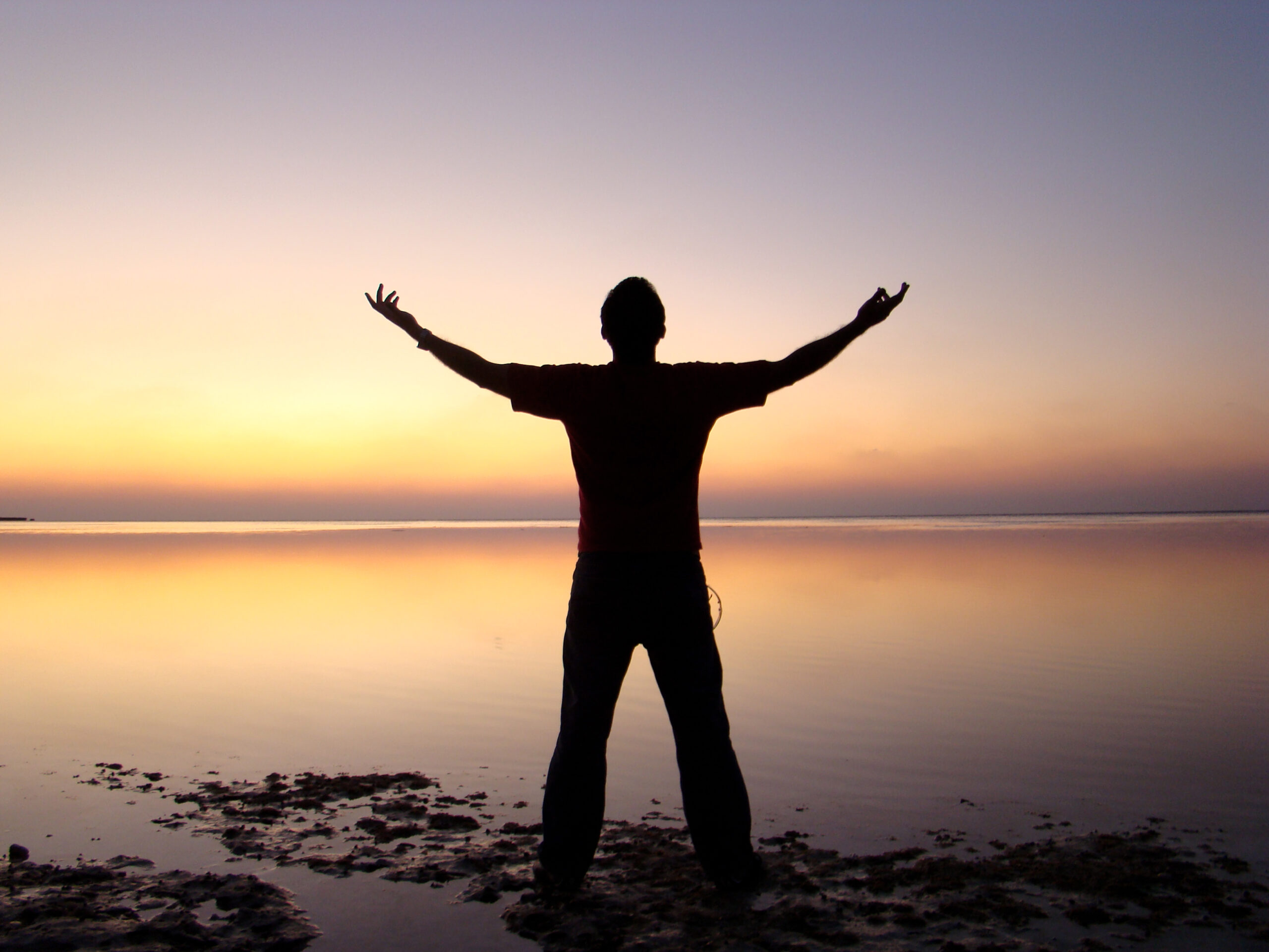 A man stands with his arms held apart, taking in the sunset.
