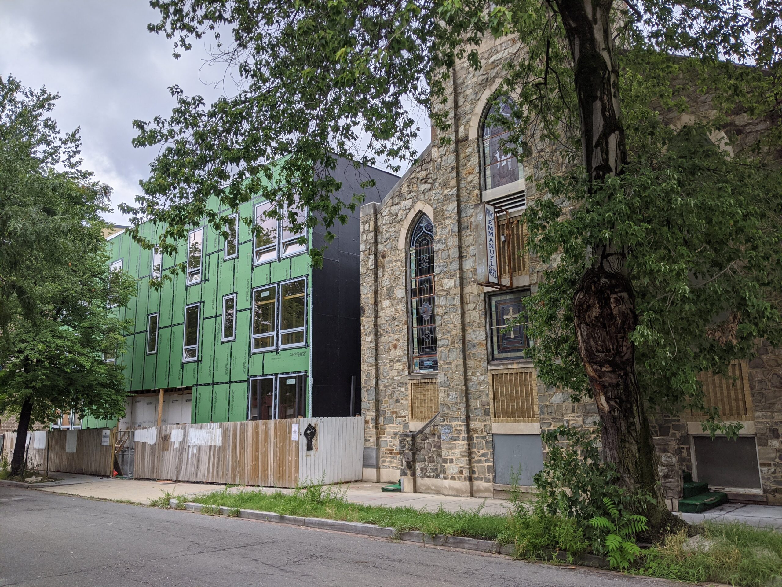 Photo showing a fenced-off construction area where a full structure has been erected, with unfinished walls masked in a green material.