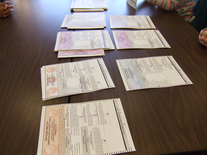 Stacks of ballots sit on a brown wood table