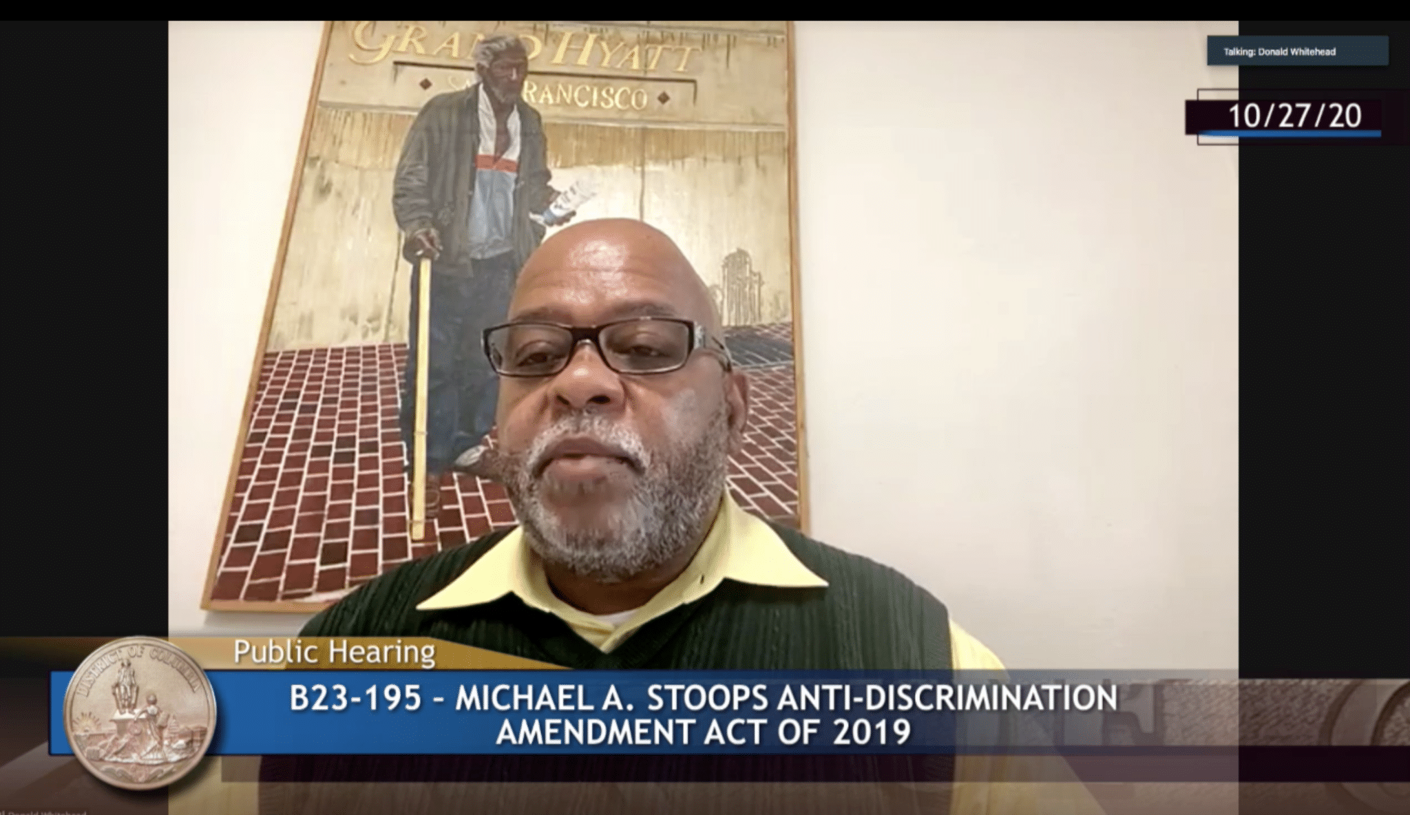 A Black man speaks on a virtual screen over a banner that reads public hearing.