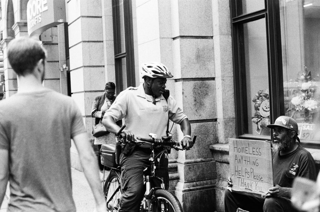 A photo of a police officer on a bike in front of a homeless person.