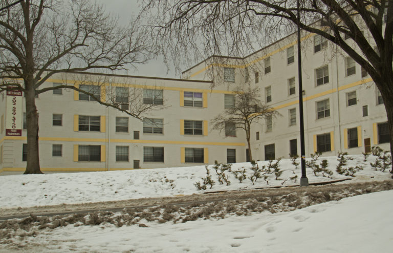 Photo of Brookland Manor ( a beige and yellow building) on a snowy day.