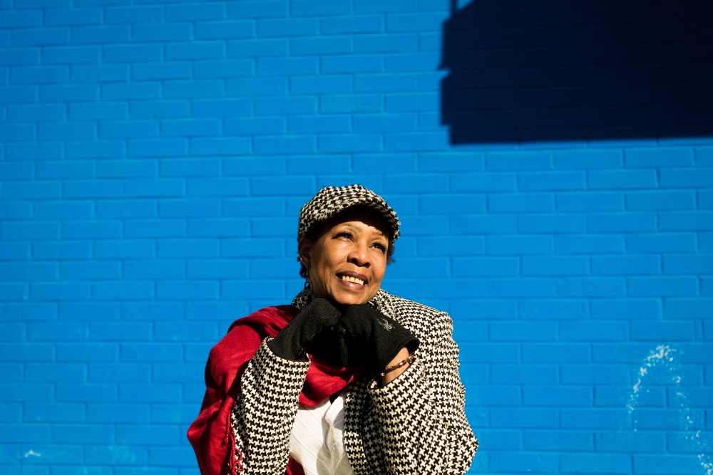 Disroe posing next to a brick wall that is painted bright blue