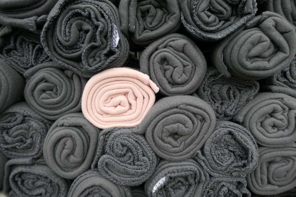 Image of several grey blankets rolled up, and one cream colored blanket, also rolled up.