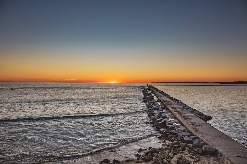 Photo of an ocean sunrise at a narrow jetty.