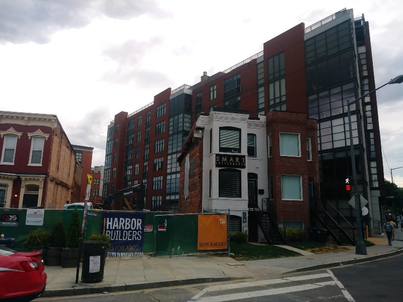Photo of a new residential building in the background, with planned redevelopment of older buildings announced in front.