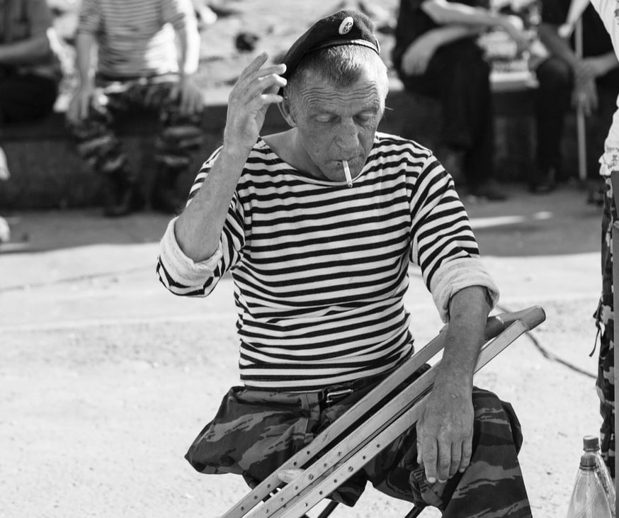 Picture of a veteran sitting on the street smoking a cigarette.